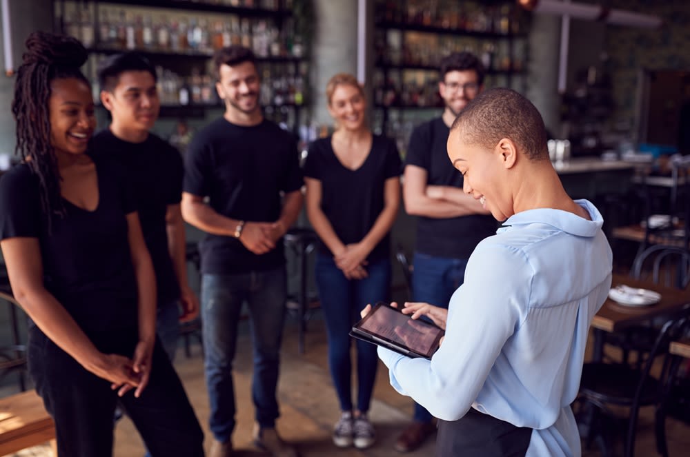 A group of wait staff talking to a manager holding a tablet