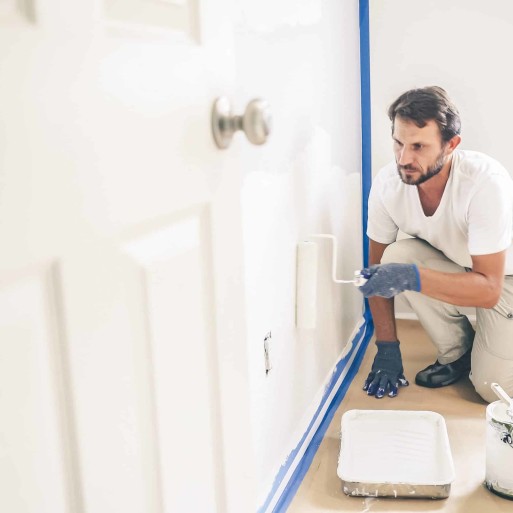 A painter in a white uniform is painting a wall using a paint roller.