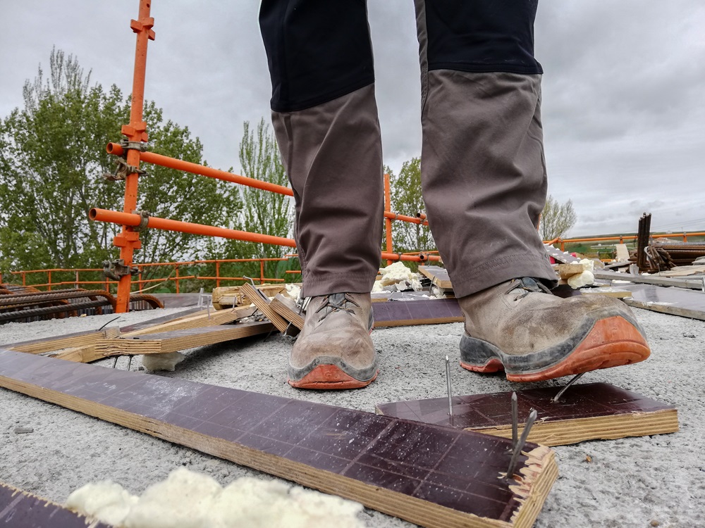 Worker about to step onto a board with exposed nails at a construction site.
