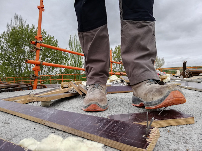 Worker about to step onto a board with exposed nails at a construction site.
