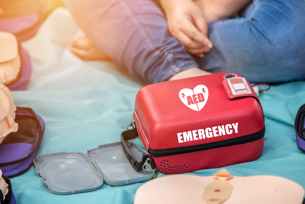 An AED kit next to a person sitting criss-cross