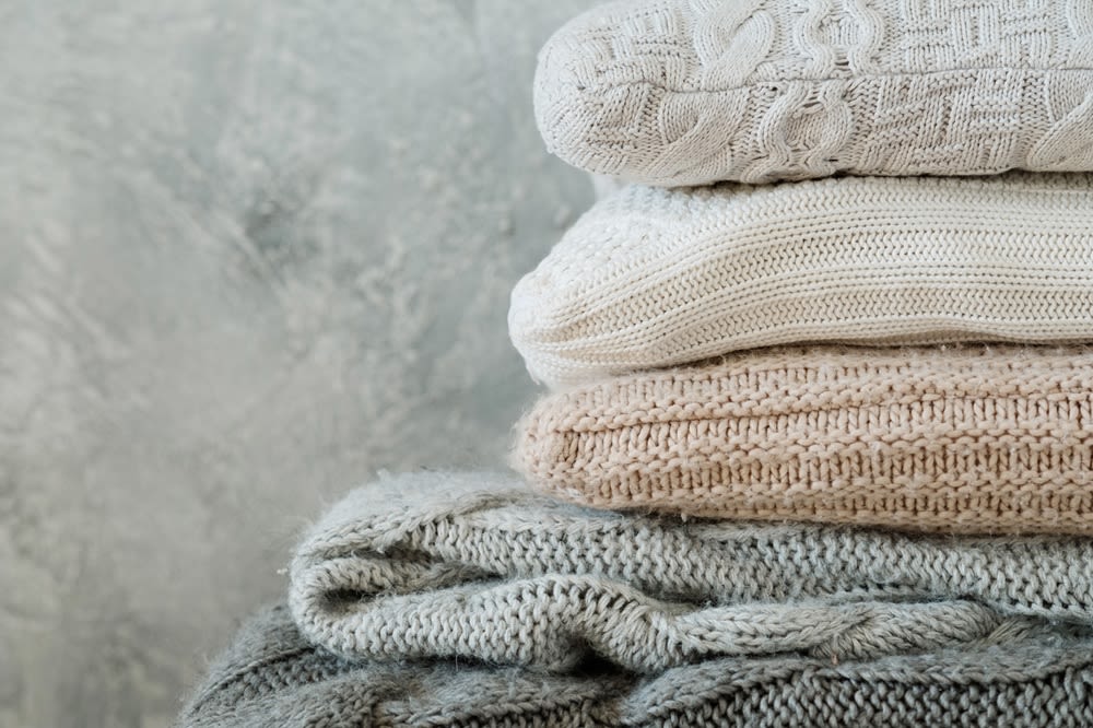 A collection of soft, plush blankets in tones of grey, white, and beige.