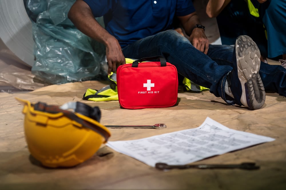 A man in an industrial work setting using a first aid kit after an accident