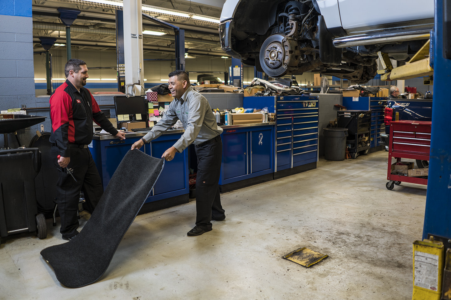 Automotive workers placing a mat on the ground.