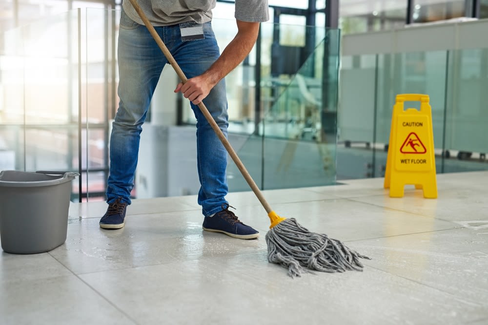 A man mopping a floor with a "Caution Wet Floor" sign near him