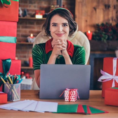 Photo of a young, female Santa's Helper sitting at a desk with a laptop