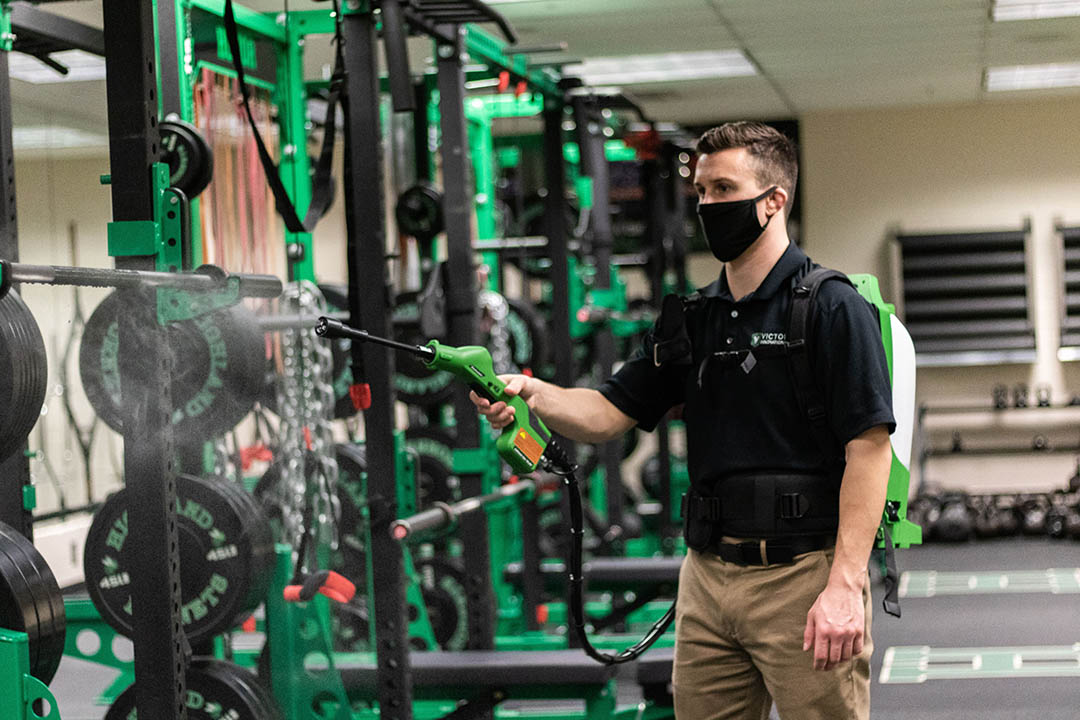 Man using a disinfectant sprayer on exercise equipment