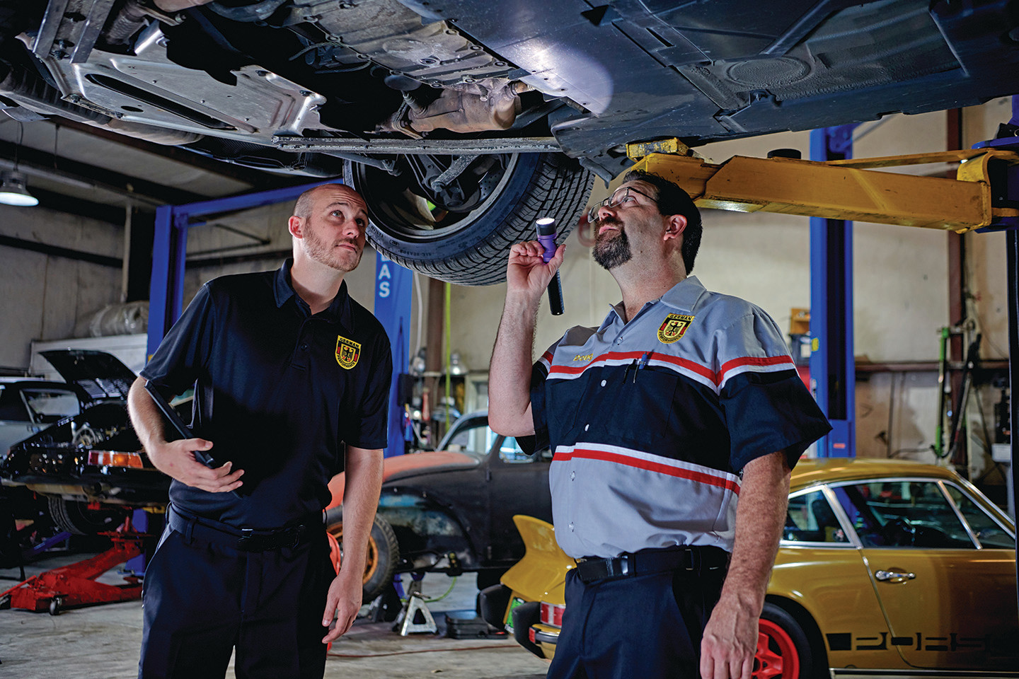 Two automotive workers inspecting the undercarriage of a car.
