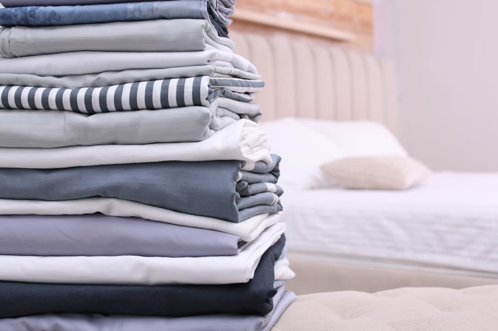 A stack of blue and grey sheets in front of an unmade bed.