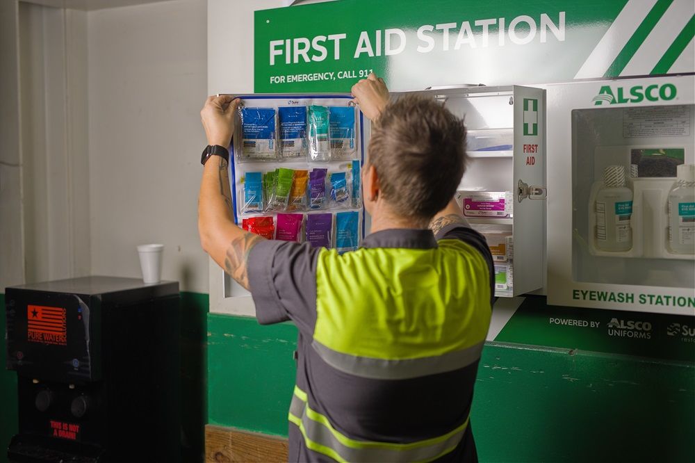 An Alsco Uniforms driver restocking a First Aid cabinet.