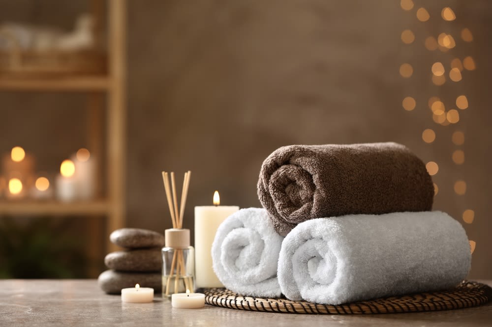 A stack of plush towels next to candles, a bundle of incense, and a pile of smooth stones.