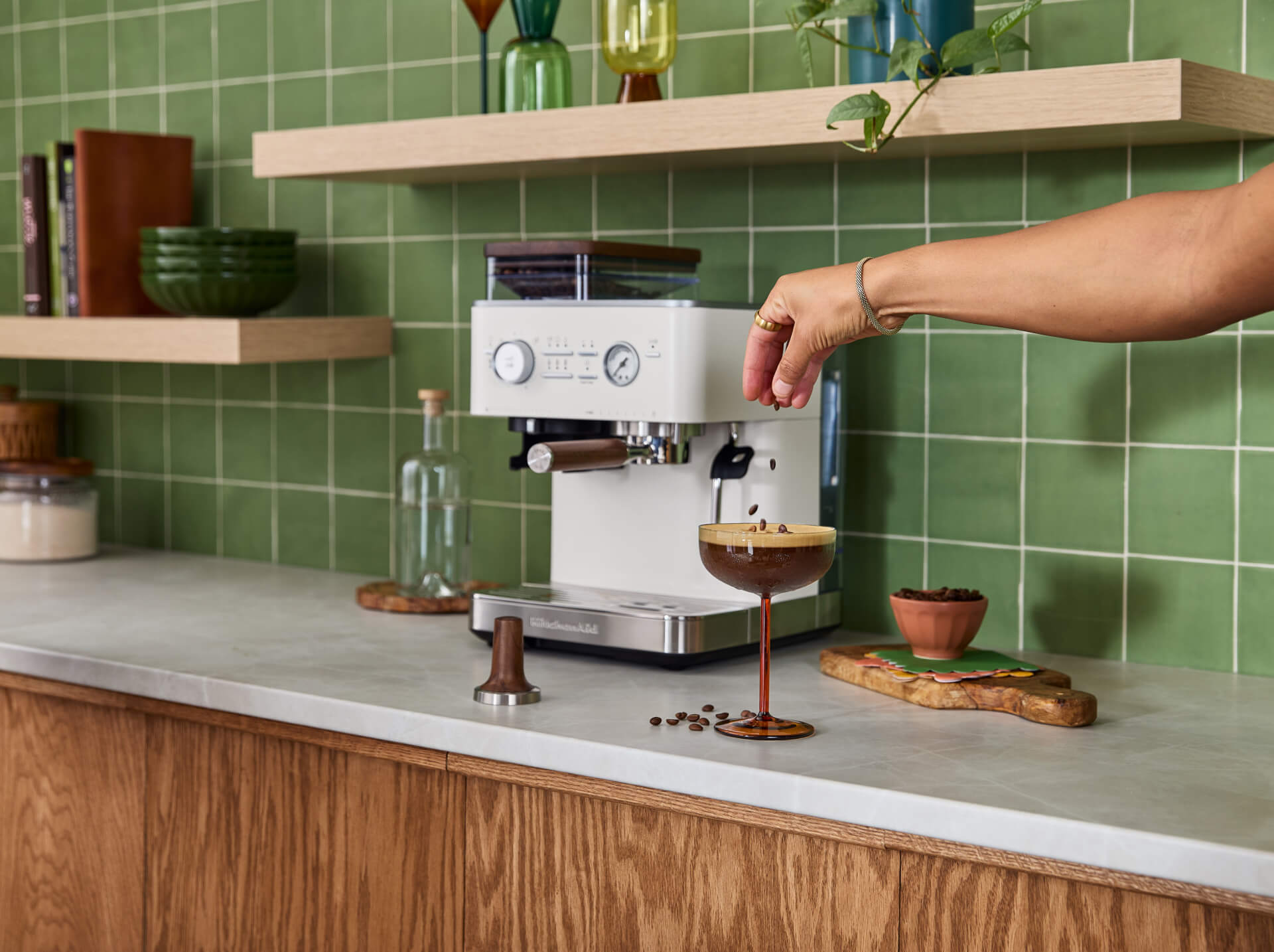 A person sprinkling espresso beans on top of a freshly made espresso martini in front of a Porcelain White espresso machine.