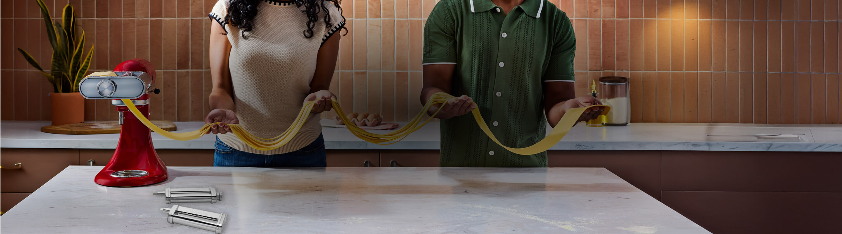 Two people making pasta with a KitchenAid® stand mixer pasta attachment