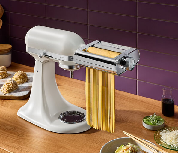 A pasta maker with fresh noodles next ot a bowl of food