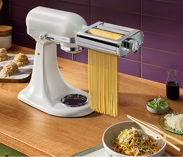 A pasta maker with fresh noodles next ot a bowl of food