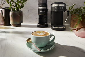 A cappuccino with KitchenAid® coffee makers in the background.