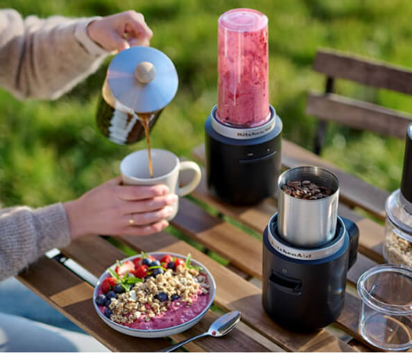A person pouring coffee into a mug with a bowl of fruit and yogurt.
