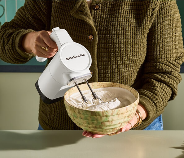 A person making dough with a cordless KitchenAid® hand mixer