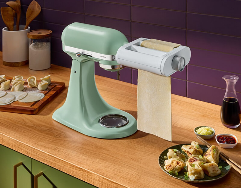A person with a Dusty Rose Stand Mixer in the foreground.