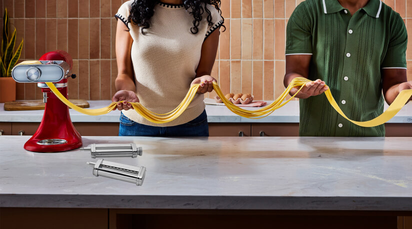 Two people making pasta with a KitchenAid® stand mixer pasta attachment