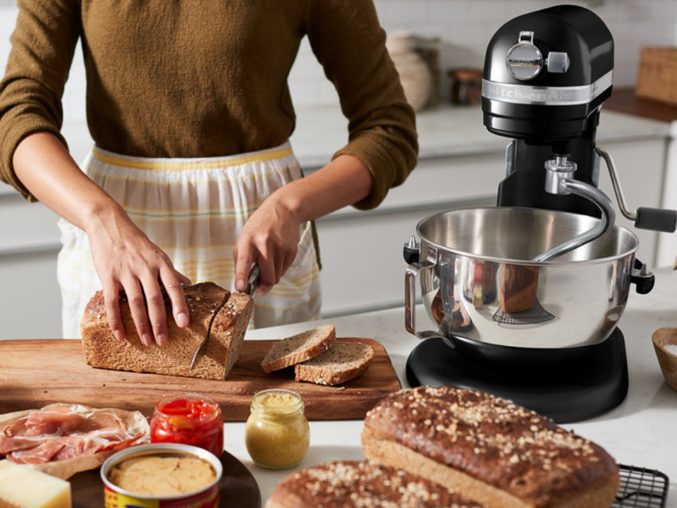 Mixers-bowl-lift-6.9L-artisan-cast-iron-black-women-cuts-bread-next-to-a-stand-mixer