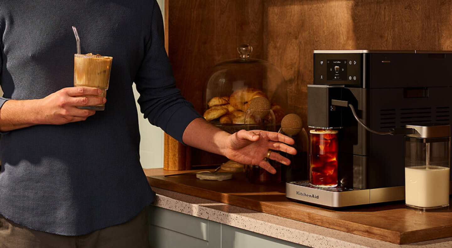 A person holding a coffee and grabbing another drink from an espresso machine