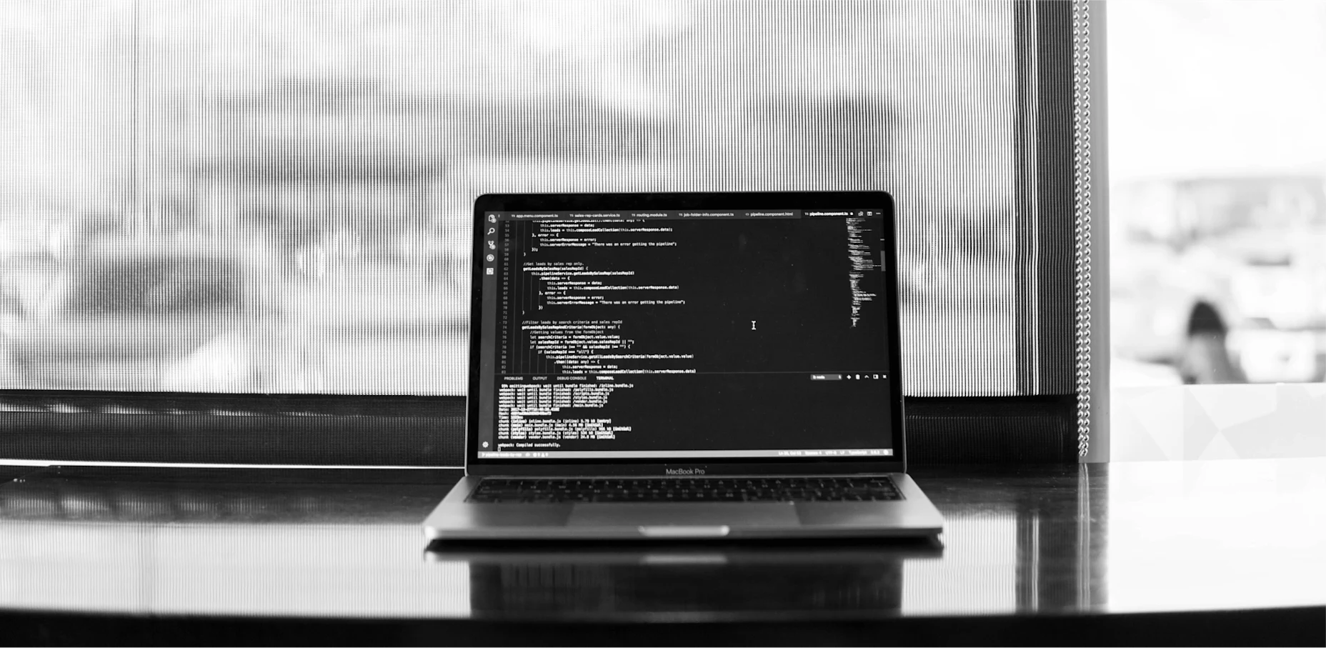 Schwarz-Weiß-Bild eines Laptops am Fenster, auf dem ein Programmiercode zu sehen ist.