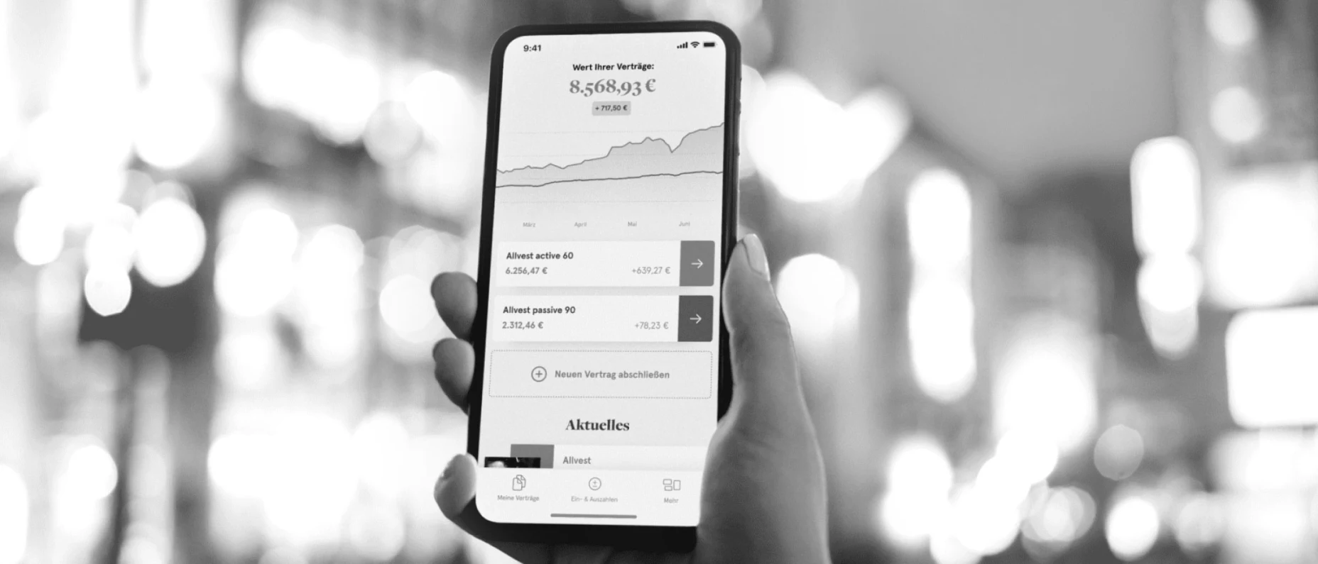 Schwarz-Weiß-Bild eines Handys mit geöffneter Allvest App und einer Stadt im Hintergrund.