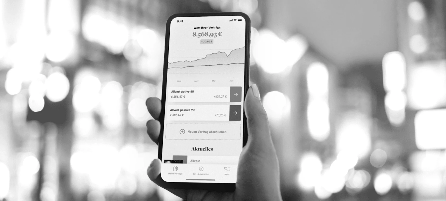 Schwarz-Weiß-Bild eines Handys mit geöffneter Allvest App und einer Stadt im Hintergrund.