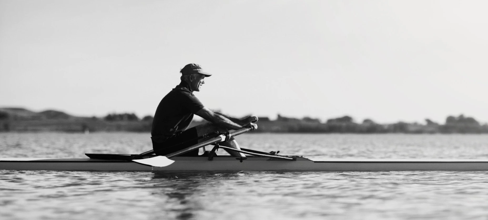Schwarz-Weiß-Bild von einem Mann im Ruderboot auf dem Wasser.