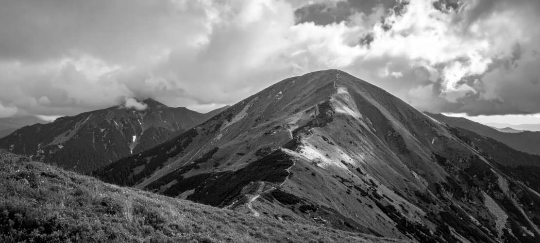 eine Bergkette mit einem schmalen Pfad unter einem wolkenverhangenen Himmel