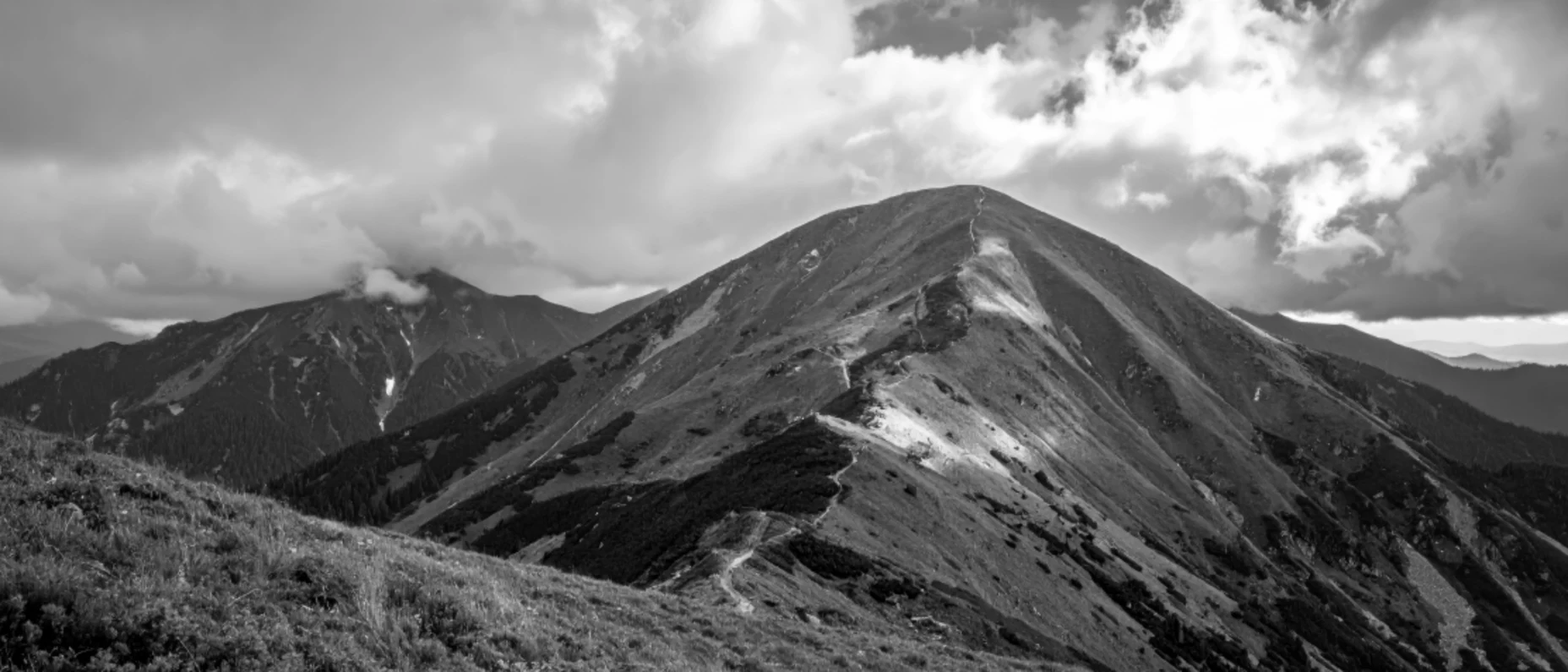 eine Bergkette mit einem schmalen Pfad unter einem wolkenverhangenen Himmel