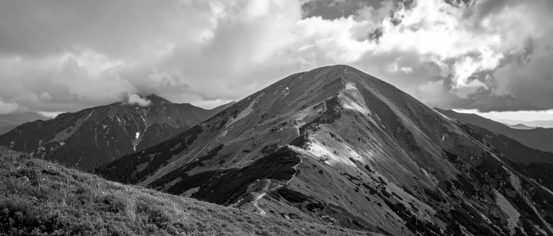 eine Bergkette mit einem schmalen Pfad unter einem wolkenverhangenen Himmel