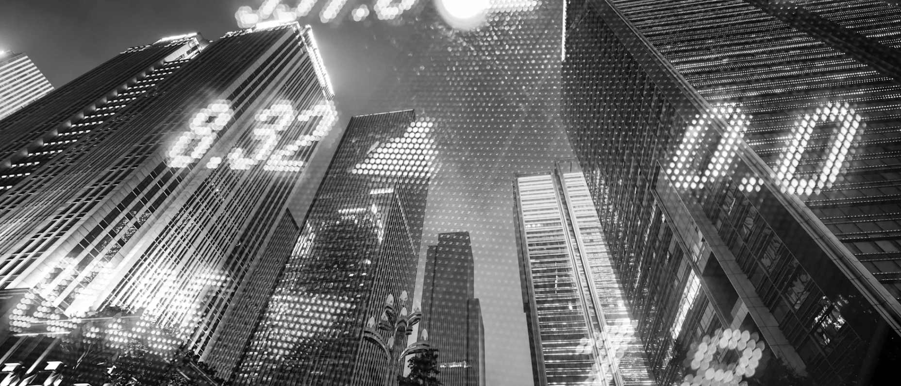 Schwarz-Weiß-Bild mit Hochhäusern im Hintergrund und eingeblendeten Börsenkurszahlen.