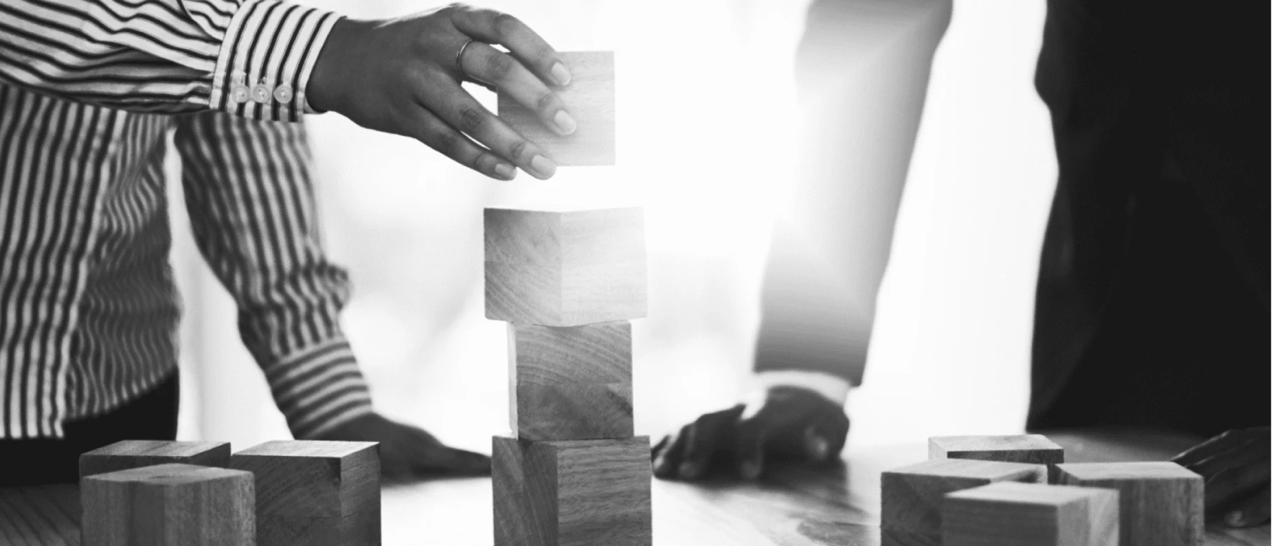 Schwarz-Weiß-Bild von zwei Personen die Holzbausteine aufeinander stapeln.