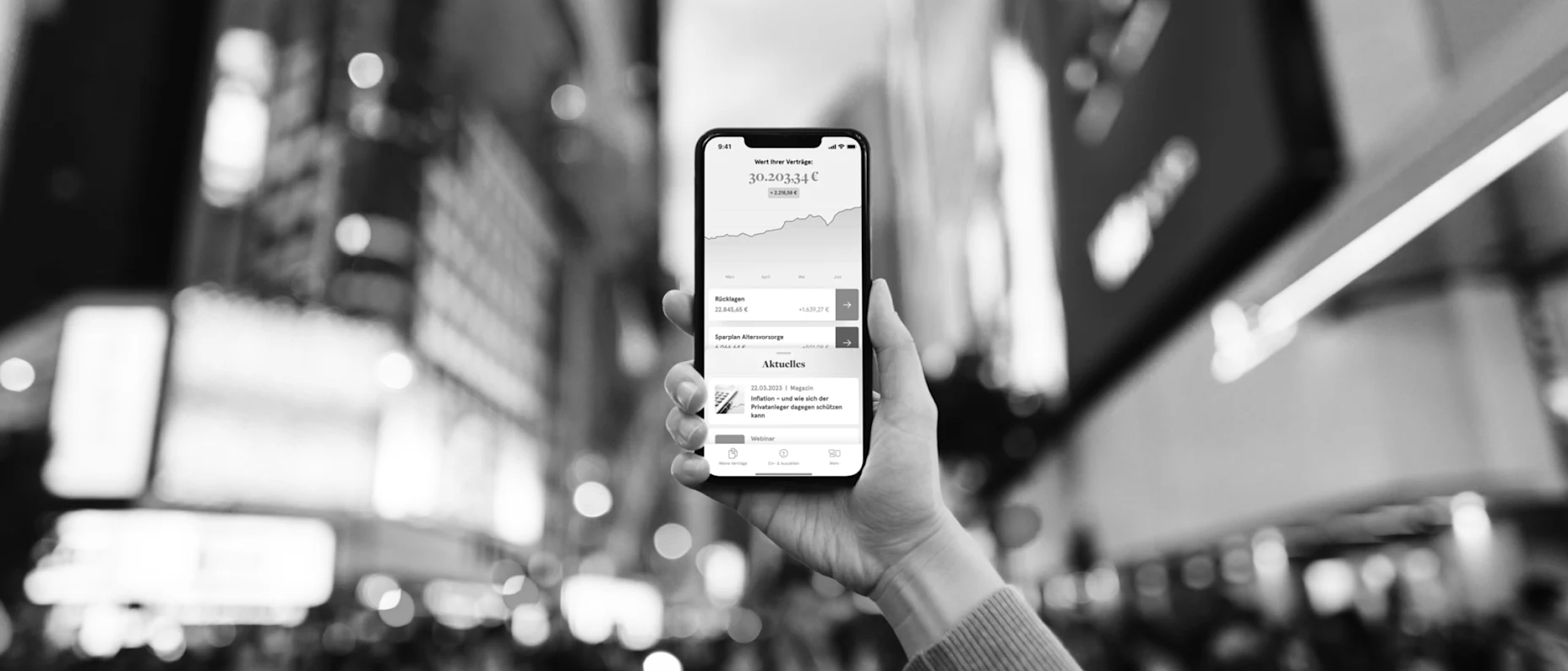 Schwarz-Weiß-Bild eines Handys mit geöffneter Allvest App und der Stadt im Hintergrund.
