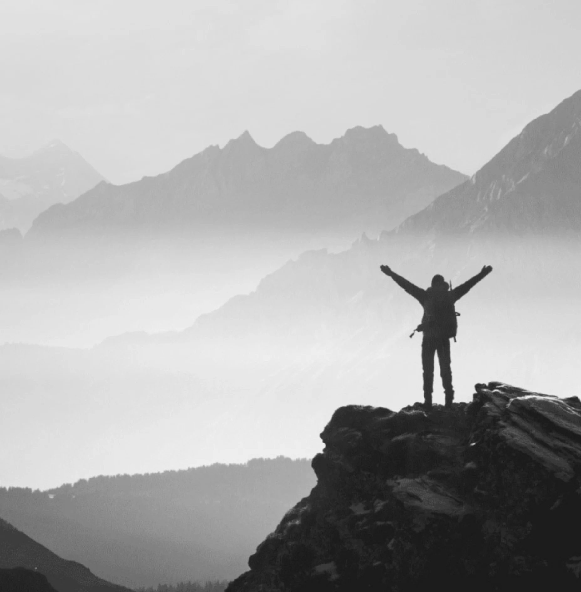 Schwarz-Weiß-Bild eines Bergsteigers auf einem Berggipfel, der die Arme in die Luft hebt.