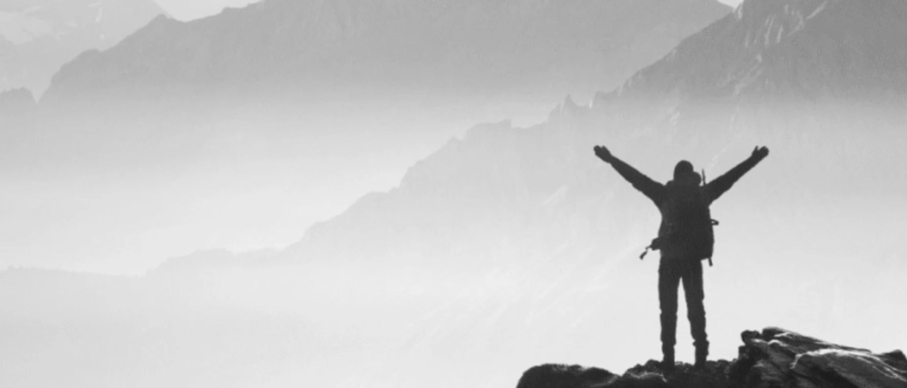 Schwarz-Weiß-Bild eines Bergsteigers auf einem Berggipfel, der die Arme in die Luft hebt.