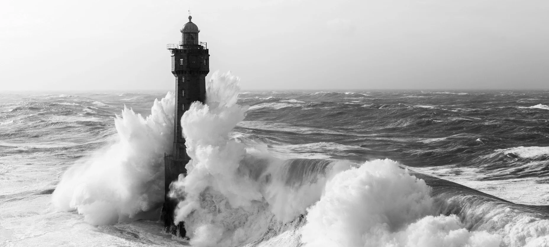 Schwarz-Weiß-Bild mit einem Leichtturm in hoher See.