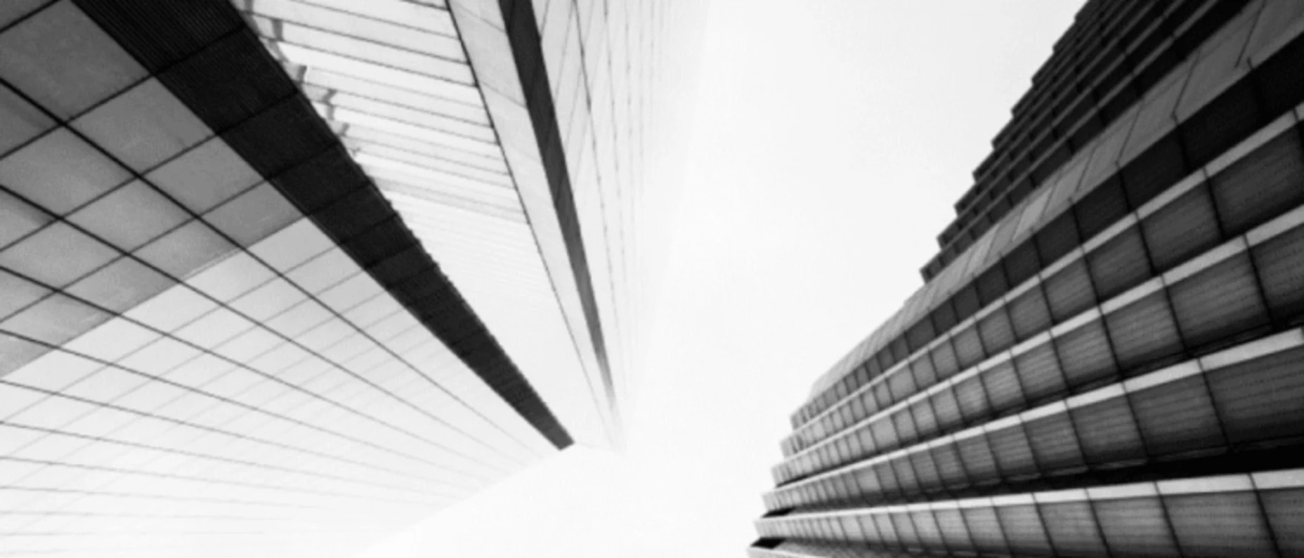 Schwarz-Weiß-Bild von zwei Hochhäusern, Aufnahme von unten mit dem Blick in den Himmel.