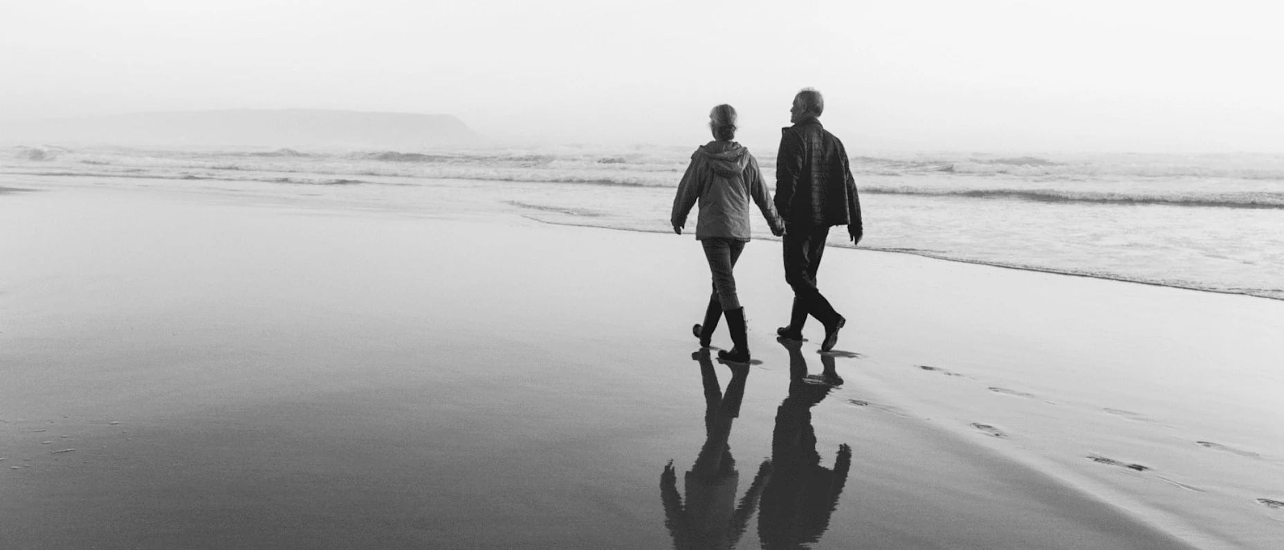 Schwarz-Weiß-Bild mit spazierenden Senioren am Strand.
