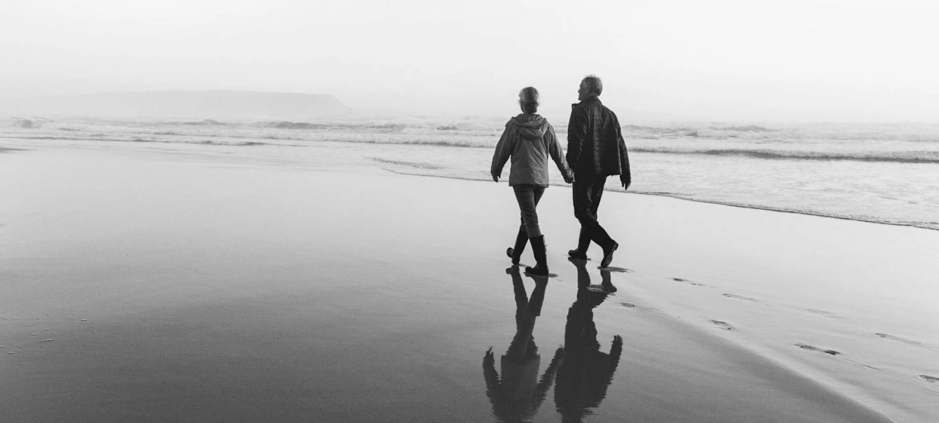 Schwarz-Weiß-Bild mit spazierenden Senioren am Strand.