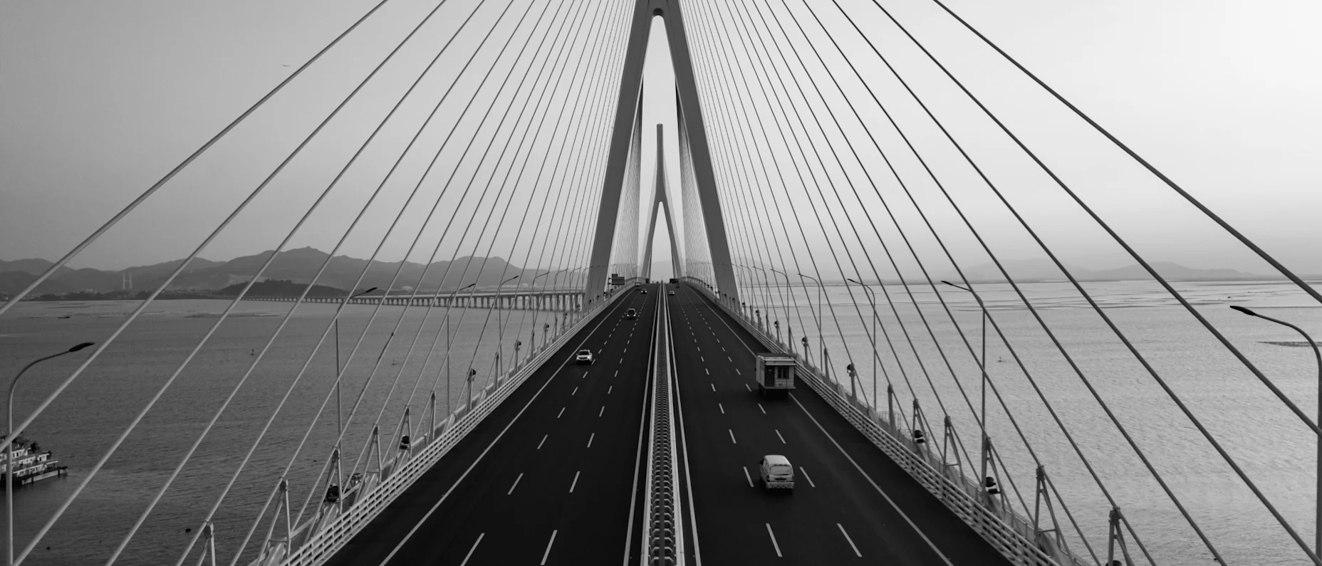 Schwarz-Weiß-Bild einer großen Brücke über Wasser, auf der von beiden Seiten Autos fahren.