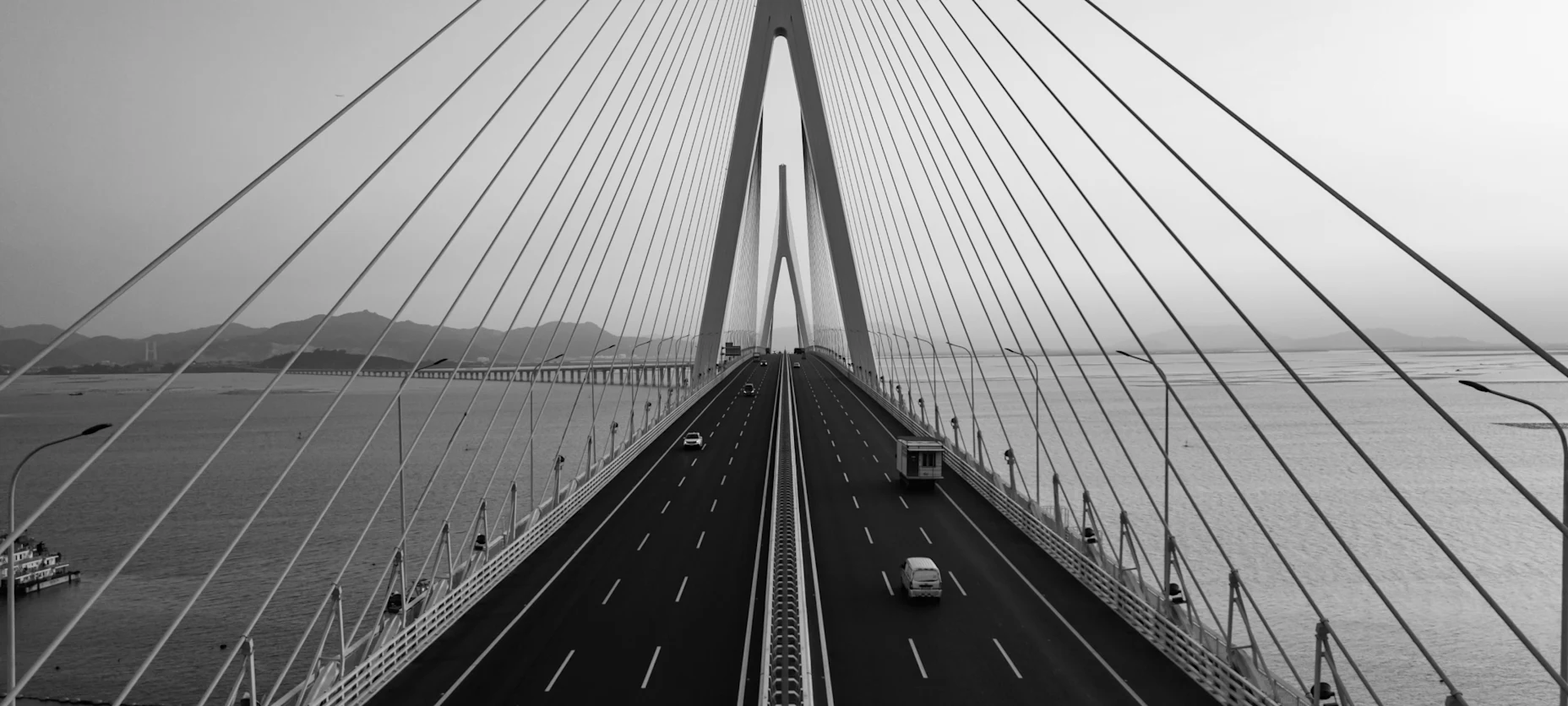 Schwarz-Weiß-Bild einer großen Brücke über Wasser, auf der von beiden Seiten Autos fahren.