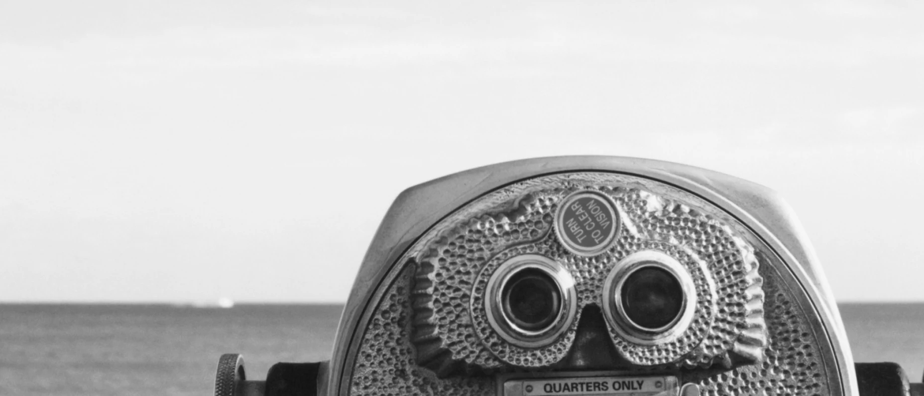 Schwarz-Weiß-Bild mit Fernglas und Meer im Hintergrund.