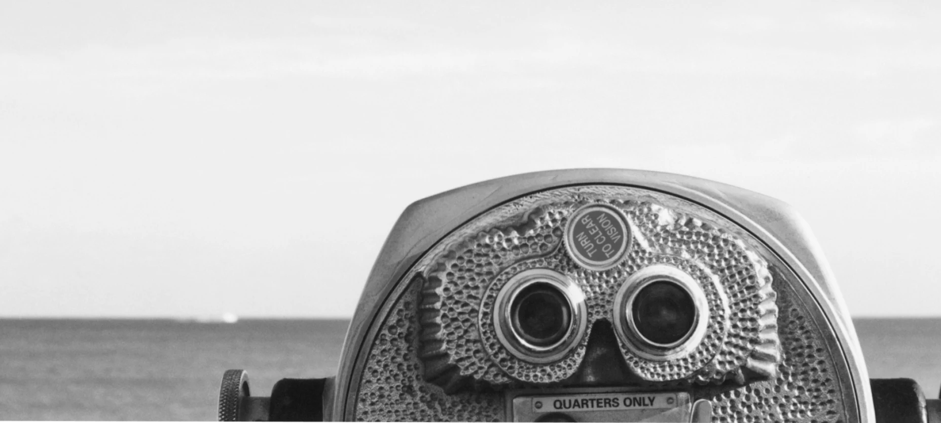 Schwarz-Weiß-Bild mit Fernglas und Meer im Hintergrund.
