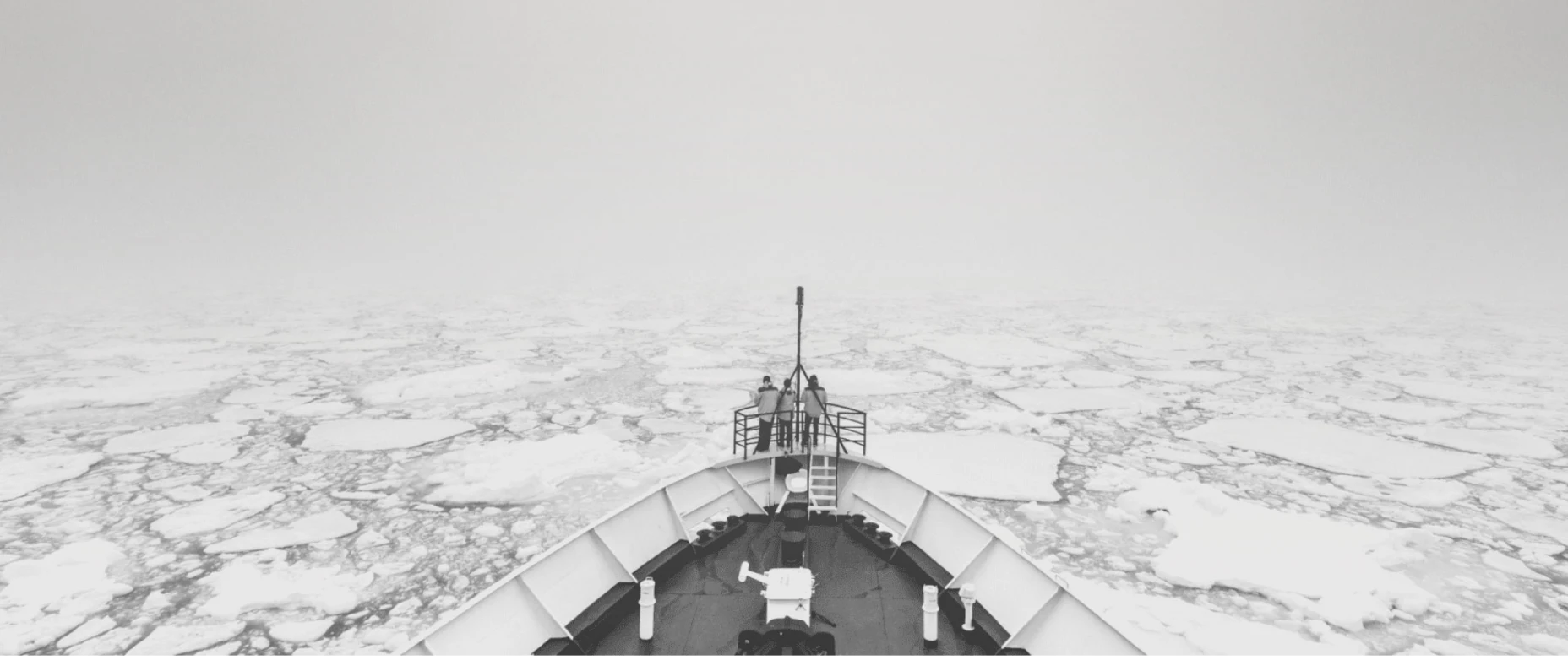 Schwarz-Weiß-Bild mit einem Eisbrecher im Meer, das durch Eisschollen fährt.