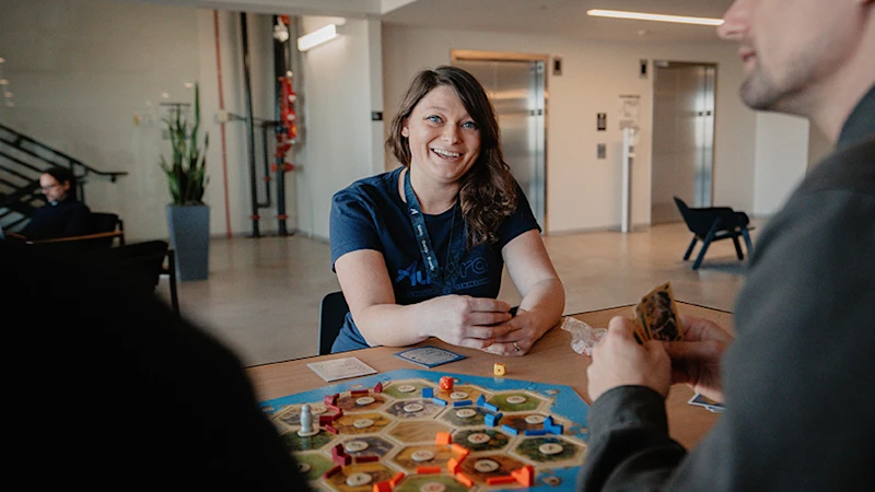 Culture Card 2 - Smiling woman sitting at table playing a board game