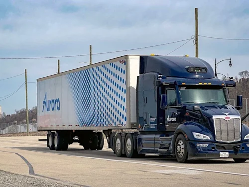 Aurora truck driving down a highway with power lines in background