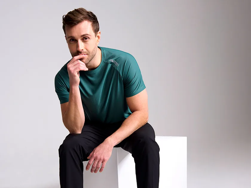 Mies poseeraa urheilukentän katsomossa istuen tummissa urheiluvaatteissa